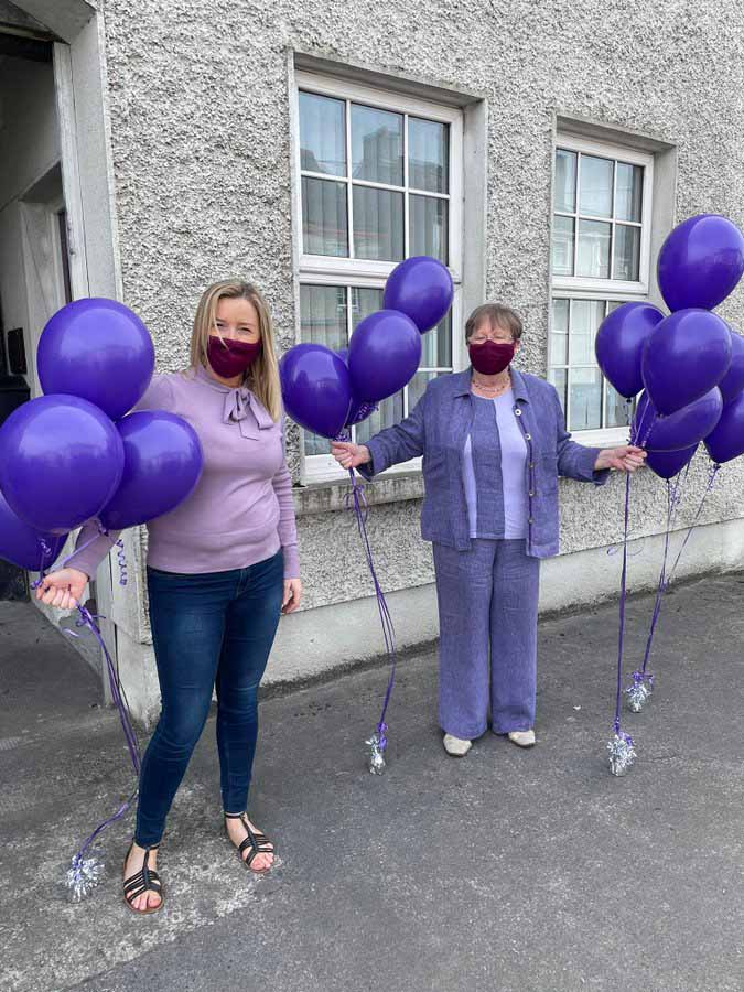 Two women dressed in purple holding purple balloons.